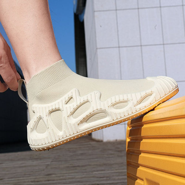 Beige sokachtige sneaker met unieke zool, gedragen door persoon op gele koffer. Moderne, comfortabele schoenen voor dagelijks gebruik.