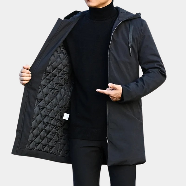 Zwarte lange herenjas met capuchon, gewatteerde binnenkant, gedragen door man in zwarte coltrui. Stijlvolle winterjas voor heren.