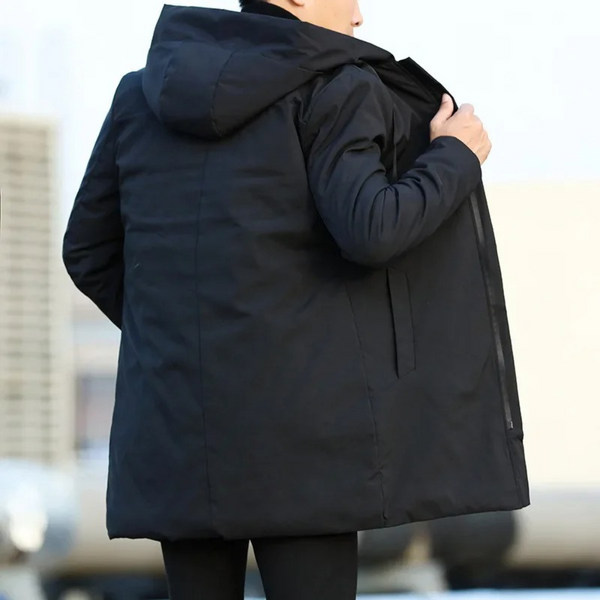Man in zwarte lange winterjas met capuchon, buiten gefotografeerd. Stijlvolle herenjas, ideaal voor koude seizoenen. Comfortabele en warme pasvorm.