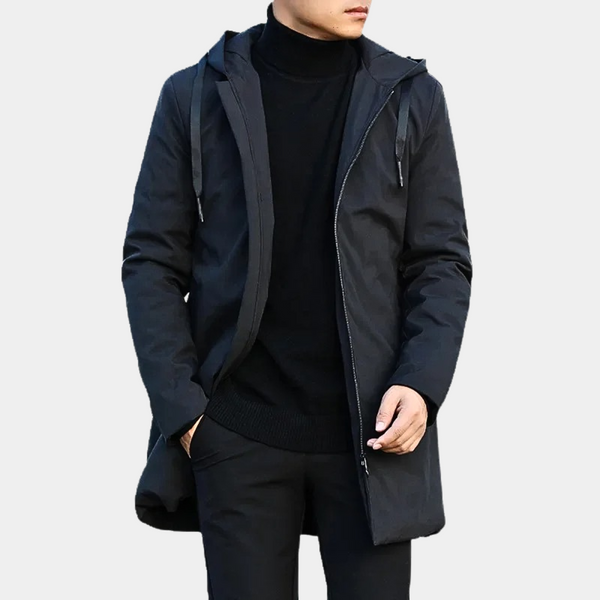 Man in zwarte lange jas met capuchon, rits en zakken, draagt zwarte coltrui en broek. Stijlvolle herenkleding, wintermode, casual outfit.