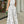 Vrouw in witte jumpsuit met abstracte zwarte lijnen, halternek en wijde pijpen, poseert buiten bij winkel. Trendy damesmode, zomeroutfit.