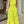 Vrouw in felgele jumpsuit met abstracte zwarte lijnen, halternek en wijde pijpen, houdt groene clutch vast. Modieuze zomeroutfit voor dames.