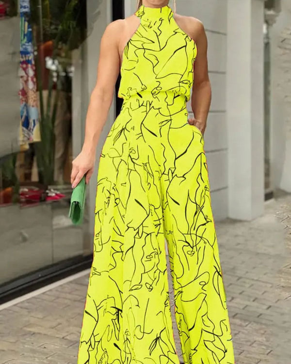 Vrouw in felgele jumpsuit met abstracte zwarte lijnen, halternek en wijde pijpen, houdt groene clutch vast. Modieuze zomeroutfit voor dames.