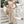 Vrouw in beige jumpsuit met knoopsluiting en strikceintuur, draagt een rieten tas. Stijlvolle zomermode, casual outfit, buitenomgeving.