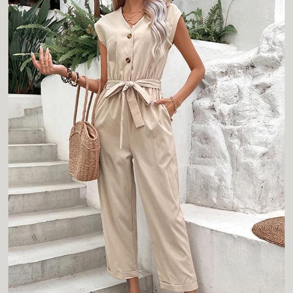 Vrouw in beige jumpsuit met knoopsluiting en strikceintuur, draagt een rieten tas. Stijlvolle zomermode, casual outfit, buitenomgeving.