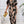 Vrouw in stijlvolle zwart-beige jumpsuit met abstract patroon, gouden clutch in hand, moderne mode, elegante outfit, trendy kledingstijl.