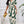 Vrouw in stijlvolle groene en witte jumpsuit met abstract patroon, gouden clutch in hand, moderne mode, elegante outfit, trendy kledingstijl.