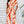 Vrouw in modieuze oranje-witte jumpsuit met abstract patroon, staand voor witte muur. Trendy dameskleding, zomeroutfit, casual chic stijl.