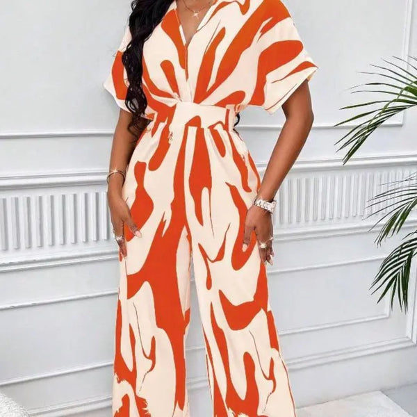 Vrouw in modieuze oranje-witte jumpsuit met abstract patroon, staand voor witte muur. Trendy dameskleding, zomeroutfit, casual chic stijl.