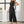 Vrouw in elegante zwarte jumpsuit met ceintuur, staand in moderne woonkamer. Stijlvolle damesmode, trendy kleding, minimalistisch design.