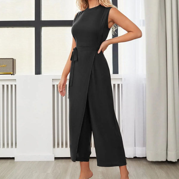 Vrouw in elegante zwarte jumpsuit met ceintuur, staand in moderne woonkamer. Stijlvolle damesmode, trendy kleding, minimalistisch design.