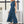 Vrouw in elegante blauwe jumpsuit met mouwloos ontwerp, staand voor raam. Trendy damesmode, stijlvolle outfit voor zomer of lente.