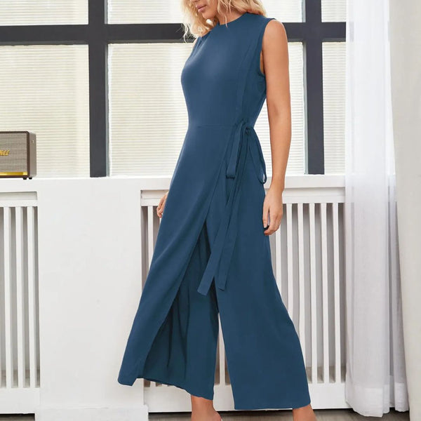 Vrouw in elegante blauwe jumpsuit met mouwloos ontwerp, staand voor raam. Trendy damesmode, stijlvolle outfit voor zomer of lente.