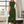 Vrouw in stijlvolle groene jurk met ceintuur, staand in moderne woonkamer. Elegante mode, trendy dameskleding, interieurdesign.