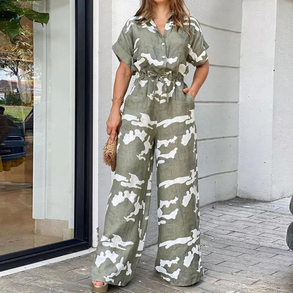 Vrouw in groene camouflage jumpsuit met korte mouwen en wijde pijpen, poseert buiten bij een winkel. Trendy damesmode, casual zomeroutfit.