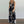 Vrouw in zwarte jumpsuit met tropische bladerenprint, mouwloos en met V-hals, staand op houten vloer. Perfect voor zomermode en casual stijl.