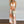 Vrouw in zomerse maxi-jurk met palmboomprint, halternek en rieten tas. Perfect voor strandmode en casual zomeroutfits.