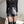 Vrouw in zwarte leren shorts en top, modieuze outfit, hoge taille, trendy kleding, moderne stijl, zwarte laarzen, minimalistisch interieur.