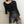 Vrouw in zwarte top met asymmetrische halslijn en hoge taille leren shorts, modieuze outfit, trendy dameskleding, minimalistisch design.