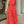 Vrouw in rode jumpsuit met abstracte zwarte lijnen, halternek en wijde pijpen, houdt groene clutch vast. Modieuze dameskleding, zomeroutfit.