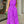 Vrouw in felroze jumpsuit met abstracte zwarte lijnen, staand voor een winkel. Ze houdt een groene clutch vast. Trendy damesmode, zomeroutfit.