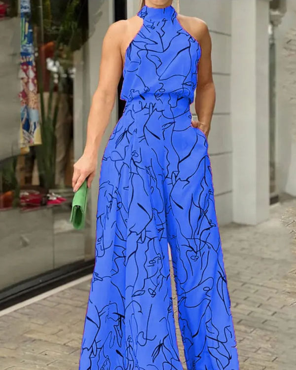Vrouw in blauwe jumpsuit met abstracte zwarte lijnen, halternek en wijde pijpen, houdt groene clutch vast. Modieuze dameskleding, zomeroutfit.