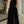 Vrouw in elegante zwarte jumpsuit met halternek, groene clutch in hand, staand op stoep voor winkel. Mode, avondkleding, stijlvolle outfit.