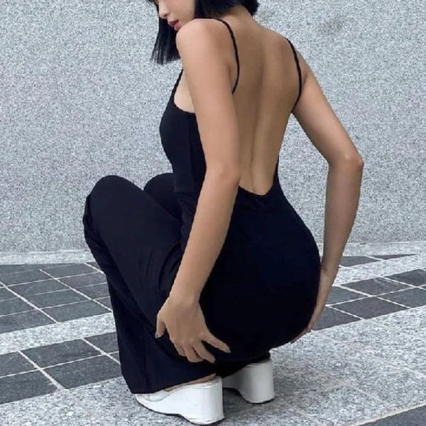 Zwarte rugloze jurk, vrouw gehurkt, witte sneakers, moderne mode, minimalistisch design, stedelijke achtergrond, trendy kledingstijl.