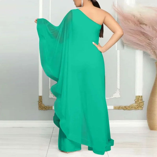 Vrouw in elegante, groene asymmetrische avondjurk met één schouder, staand in moderne interieursetting. Perfect voor galafeest of bruiloft.