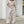 Vrouw in beige-witte jumpsuit met abstract patroon, korte mouwen en wijde pijpen, poseert buiten voor een moderne winkelgevel.