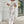 Vrouw in beige-witte linnen jumpsuit met camouflageprint, wandelend op stoep voor winkel. Modieuze dameskleding, casual zomeroutfit.