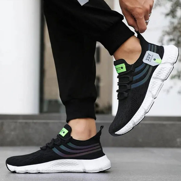 Zwarte sportschoenen met witte zool, groene accenten en gestreept design, gedragen door een persoon. Perfect voor hardlopen en casual gebruik.