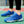 Blauwe tennisschoenen met witte driehoekige patronen op een tennisbaan, naast een tennisracket. Perfect voor sport en outdoor activiteiten.