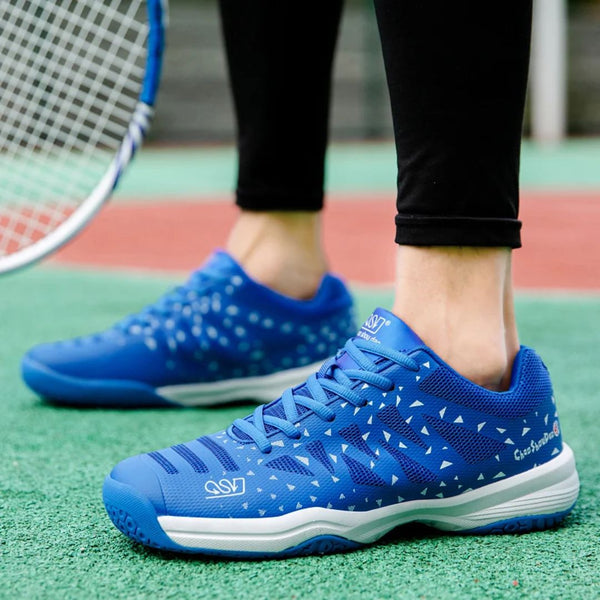 Blauwe tennisschoenen met witte driehoekige patronen op een tennisbaan, naast een tennisracket. Perfect voor sport en outdoor activiteiten.