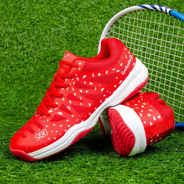 Rode tennisschoenen met witte driehoekige patronen op kunstgras, naast een tennisracket. Ideaal voor sport en outdoor activiteiten.