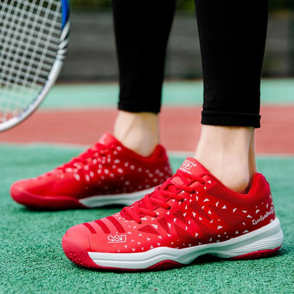 Rode tennisschoenen met witte patronen op een groene tennisbaan, naast een tennisracket. Ideaal voor sport en outdoor activiteiten.