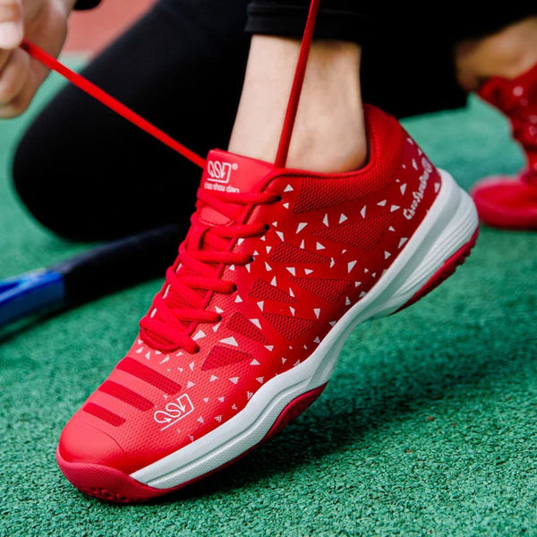 Rode sportschoen met witte driehoekige patronen, veters strikken, op groene ondergrond. Ideaal voor tennis, hardlopen, fitness. Comfortabel en stijlvol ontwerp.