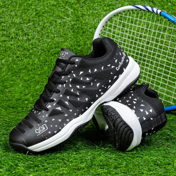 Zwarte tennisschoenen met witte driehoekige patronen op kunstgras, naast een tennisracket. Perfect voor sport en outdoor activiteiten.