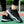 Zwarte tennisschoenen met witte driehoekige patronen, gedragen op een tennisbaan. Comfortabele sportschoenen voor optimale prestaties.