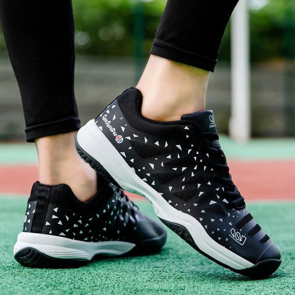 Zwarte tennisschoenen met witte driehoekige patronen, gedragen op een tennisbaan. Comfortabele sportschoenen voor optimale prestaties.