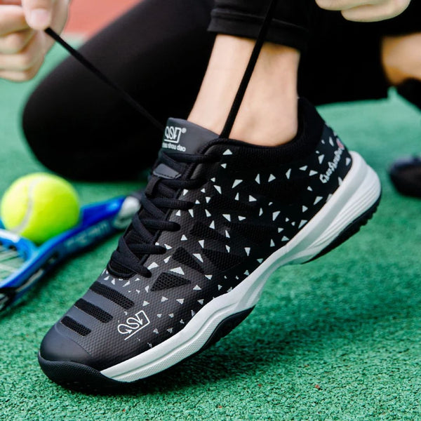 Zwarte tennisschoen met witte driehoekige patronen, naast een tennisracket en bal op groene ondergrond. Perfect voor sport en outdoor activiteiten.