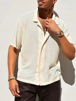 Stijlvolle man in crèmekleurig gehaakt overhemd, korte mouwen, zwarte broek, gouden horloge en armband, tegen witte achtergrond. Zomermode heren.