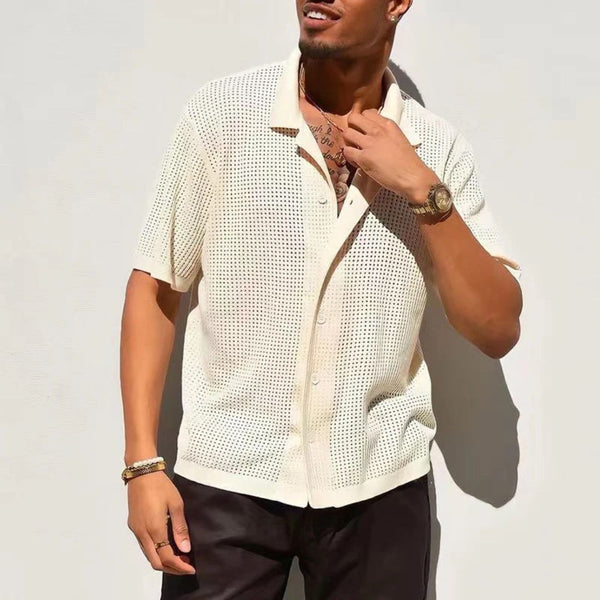 Stijlvolle man in crèmekleurig gehaakt overhemd, korte mouwen, zwarte broek, gouden horloge en armband, tegen witte achtergrond. Zomermode heren.