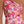 Vrouw in roze en oranje bloemenjurk met asymmetrische halslijn, elegante zomerjurk, modetrend 2024, stijlvolle dameskleding.