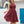 Vrouw in elegante bordeauxrode kanten jurk, halternek, zwierige rok, voor witte en blauwe mediterrane achtergrond. Perfect voor zomerfeesten.