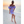 Vrouw in lila off-shoulder jurk met ruches loopt op tropisch strand bij zonsondergang. Zomermode, strandkleding, elegante jurk, vakantie.