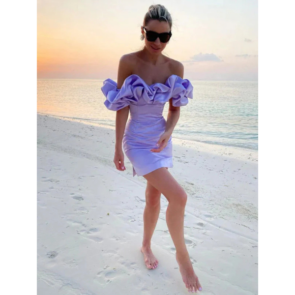 Vrouw in lila off-shoulder jurk met ruches loopt op tropisch strand bij zonsondergang. Zomermode, strandkleding, elegante jurk, vakantie.