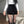 Vrouw in witte trui en zwarte corduroy shorts, hoge taille, poseert in moderne woonkamer. Modetrend, herfstkleding, stijlvolle outfit.