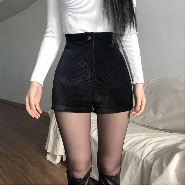 Vrouw in witte trui en zwarte corduroy shorts, hoge taille, poseert in moderne woonkamer. Modetrend, herfstkleding, stijlvolle outfit.