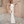 Elegante vrouw in witte avondjurk met kralenkettingen, staand op stenen pad voor beige muur. Perfect voor galajurk, mode, avondkleding.
